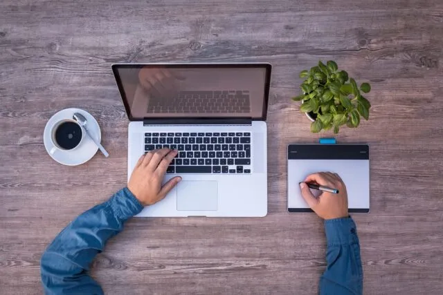 Caiet deschis și laptop pe un birou de lucru, cu o cană de cafea alături